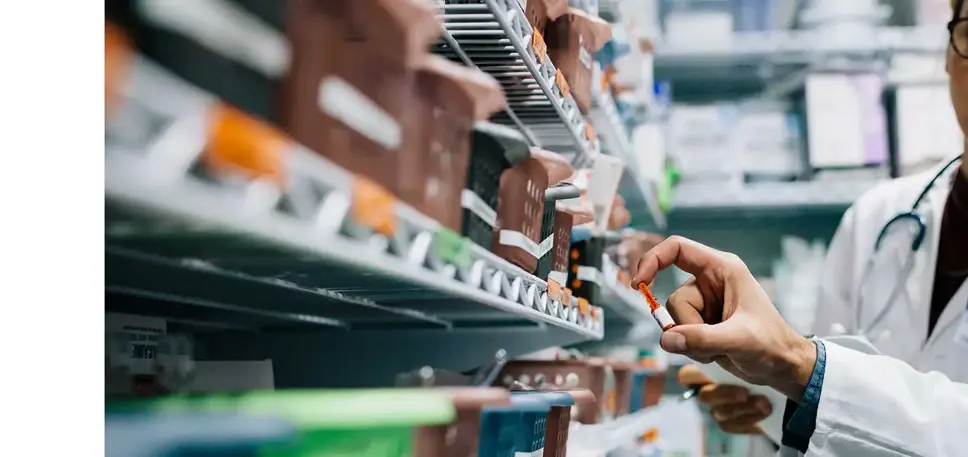 Two pharmacists face a full prescription medicines rack, while examining one particular medicine