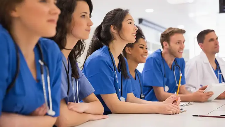 A line of seated doctors in blue uniform are being briefed.