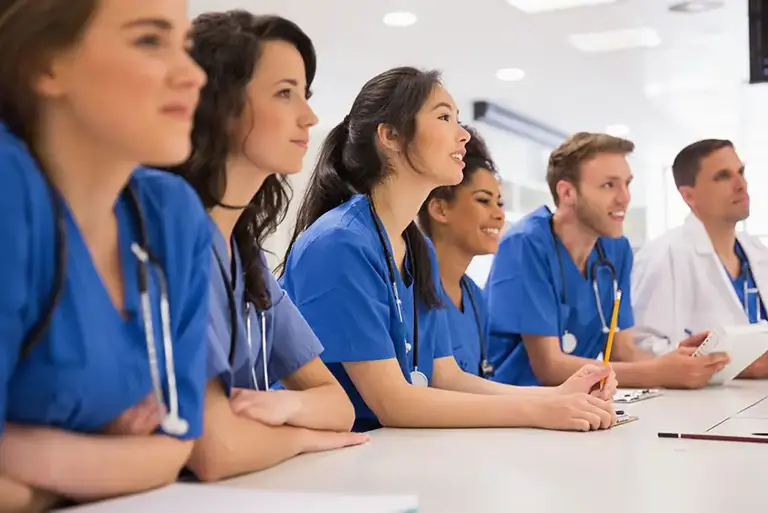 A line of seated doctors in blue uniform are being briefed.