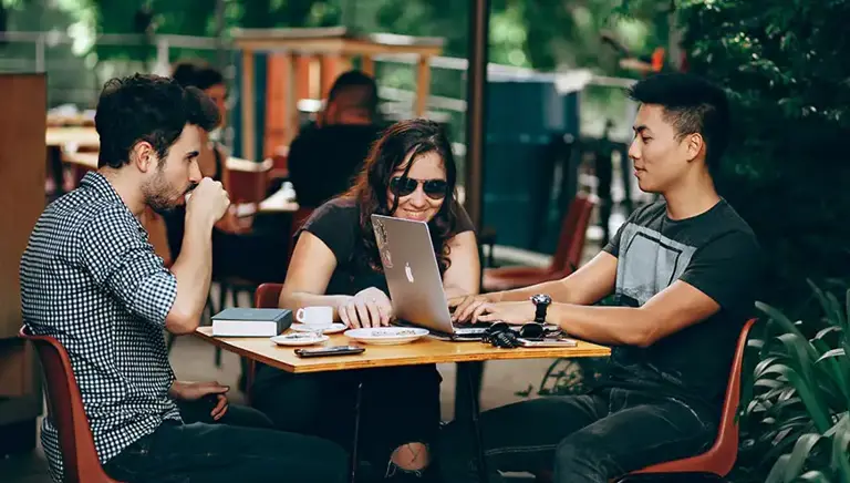 Three young causally dress workers sit working at a small table outside a glass fronted coffee shop