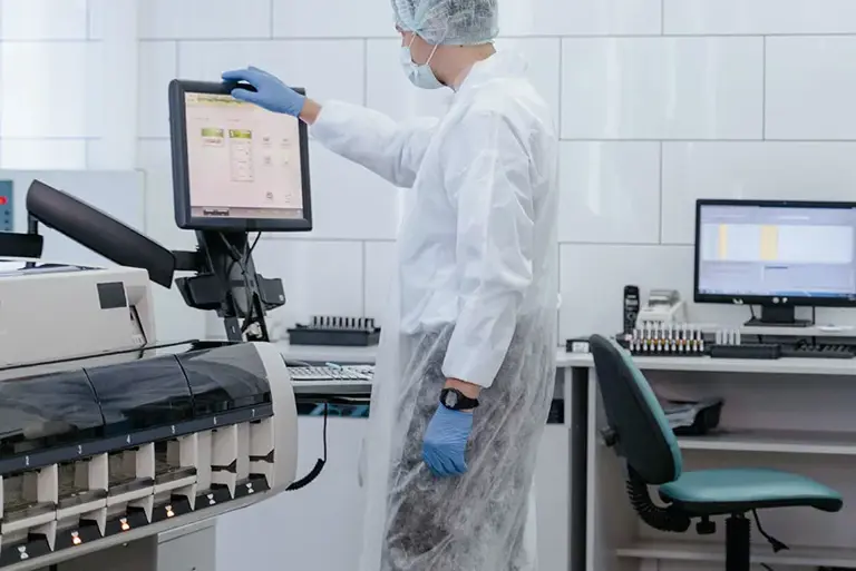 Scientist stands in a lap working at a computer screen attached to a large machine 