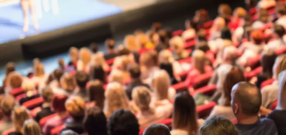 View from the back of packed auditorium with looking towards the speaker on the stage below 