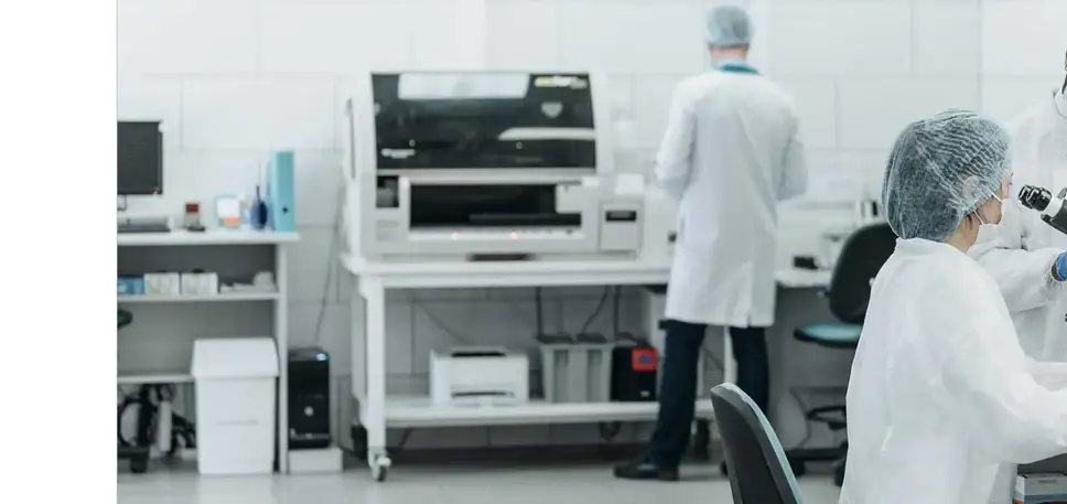 Three scientists working in a lab in conversation while one looks through a microscope