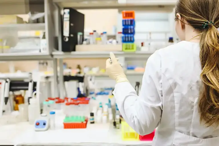 View from behind of a scientist working on a chemical bench, with a pipette. 