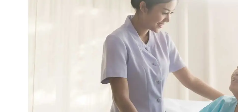 Standing healthcare professional smiles down to an seated older female patient who smiles warmly in return