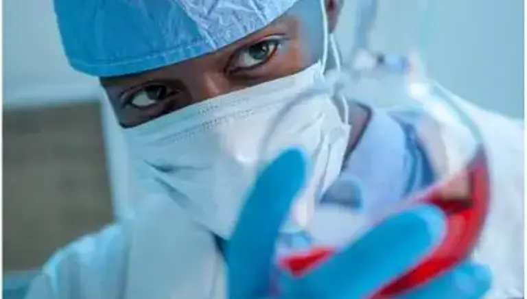 A masked scientist holds a chemical glass flask full of liquid