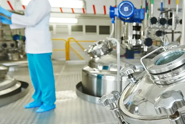 Scientist in the background, with huge stainless steel vats in the foreground 