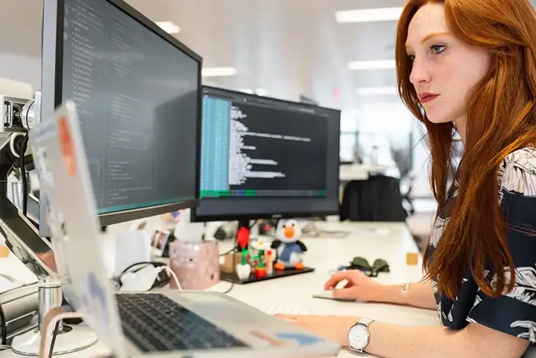 Office worker carefully looking over code across two screens 