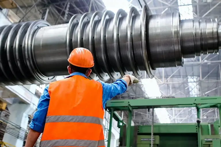 View from behind of a heavy plant worker looking up to a massive steel spindle