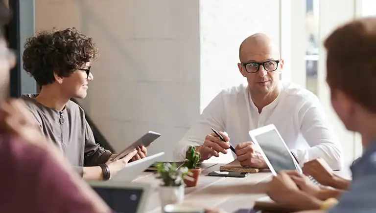 A team of casually dressed office workers sit a large desk having a meeting 