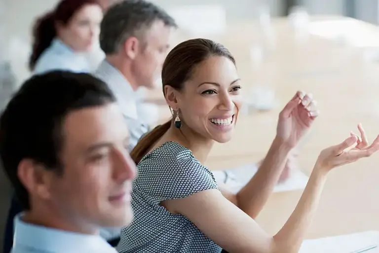 Woman at a meeting, sits smiling at the unseen delegates