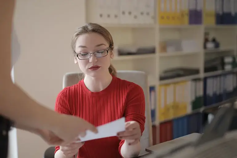 Seated office worker with library shelves of different coloured leverage arch files/records behind her