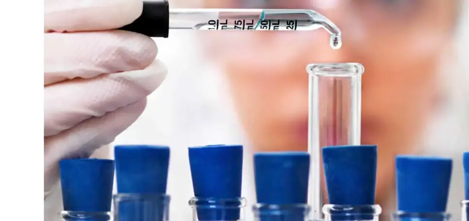 Close up of a rack of test tubes with a scientist adding a single drop from a pipette into the middle test tube.