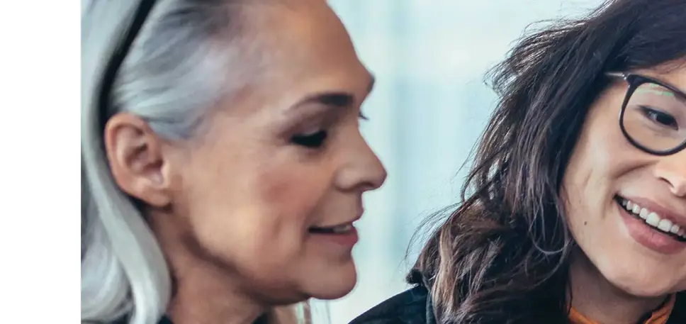 Close-up of the face of two women in conversation, one in her late 20, wearing glasses, the other is older with grey hair